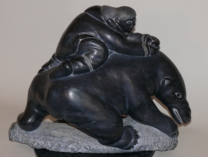 Lucassie Echalook, Hunter attacking bear with knife, c. 1970
15 x 17 x 8 in.
This dramatic, dynamic carving shows a hunter clinging to the back of a bear, with his knife embedded in the bear's back.  
Lucassie Echalook was raised on the land, and this carving vividly conveys the intensity of the hunter's struggle with the bear.  It is unusual in Lucassie's oeuvre for its extensive negative space.  It is also distinctive among many Inukjuak carvings for being fully realized in the round.  It does not have an obvious "front" and "back" -- as you rotate it, the composition has interest when viewed from any angle.
03705-1